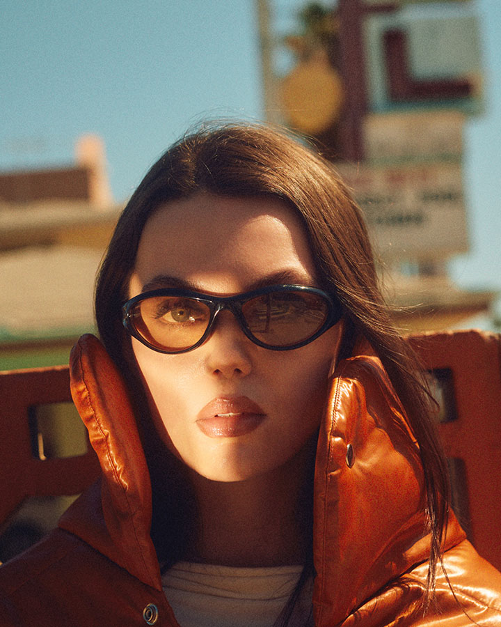 Close up portrait of Caroline Cummings in sunglasses with a beam of light across her face as she makes eye contact with the camera